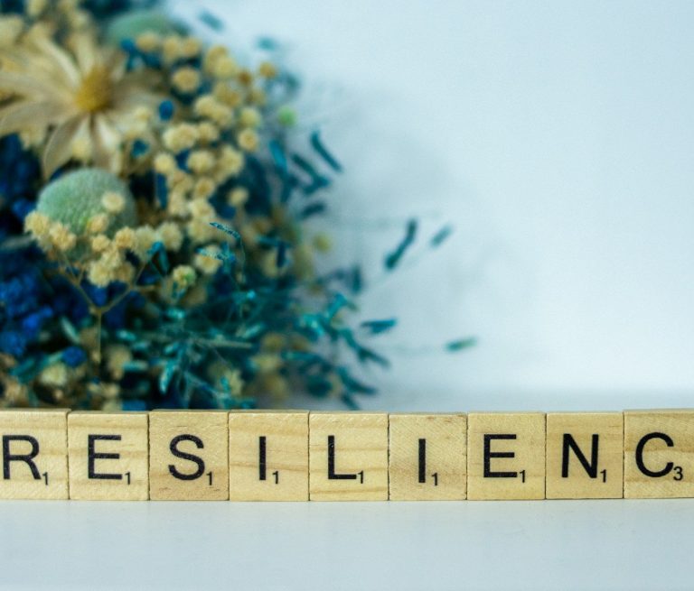 Holzbuchstaben schreiben "RESILIENT" vor einer bunten Trockenblumenarrangement.